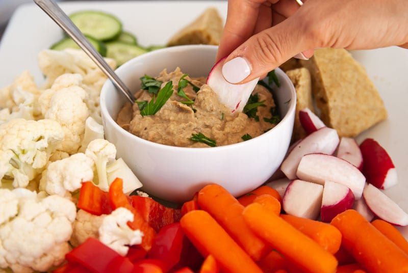 Dipping radish into a roasted eggplant dip