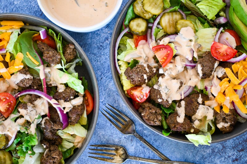 Overhead shot of 2 Cheeseburger Salad with Thousand Island Sauce on blue backgound