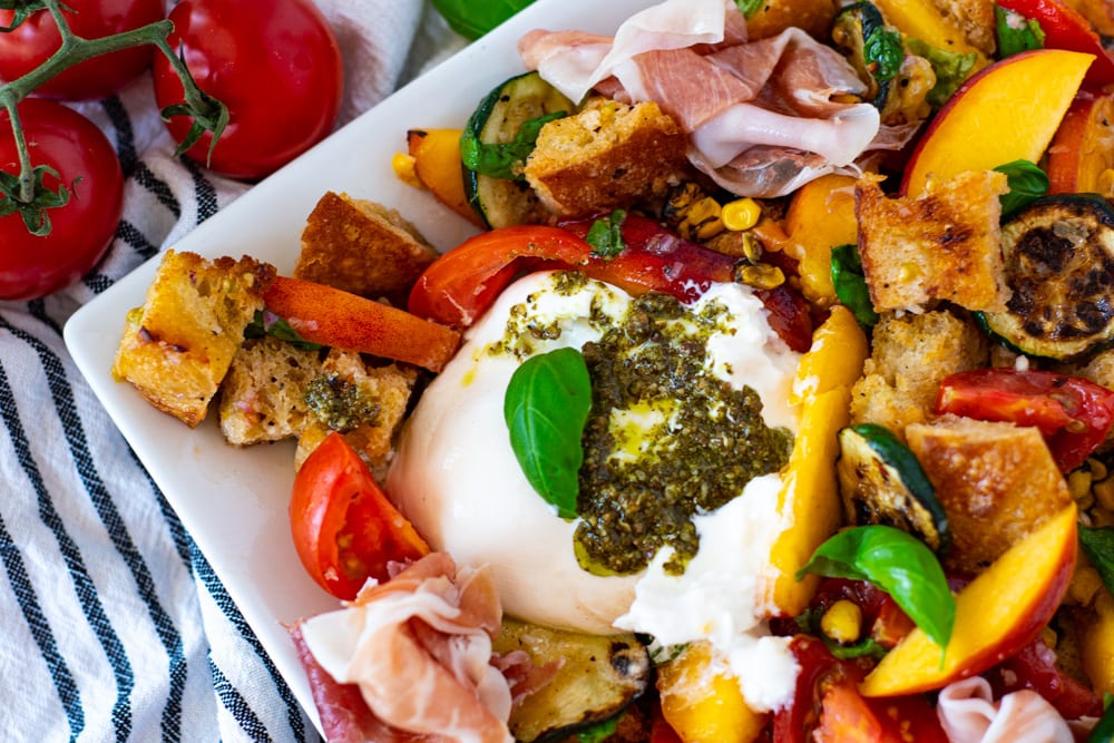 Close up of Pesto Smothered Burrata on top of a Summer Panzanella Salad with homemade croutons